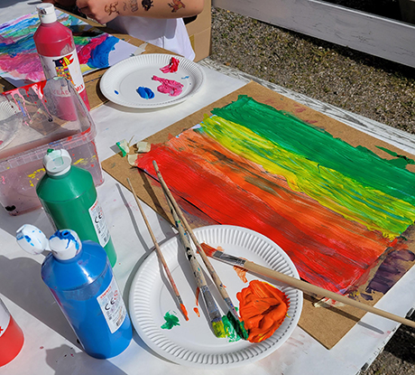 Konstverk i starka färger. På bordet står färgburkar och en palett. Vid bordet sitter ett barn och målar.