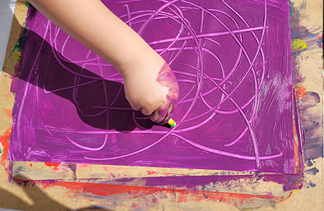 Konstverk i lila färg, en arm som målar med pastellkrita över hela pappret
