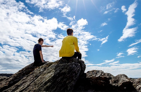 Två killar sitter på toppen av en klippa och spanar över landskapet