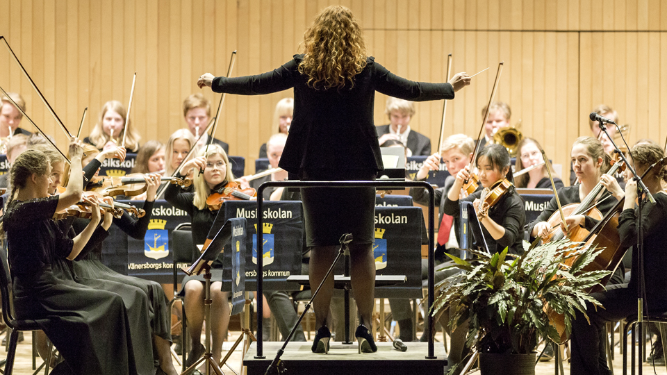 Musikskolans stråkorkester uppträder på scen med en dirigent i mitten.