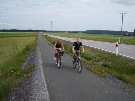 Bilden föreställer två personer som cyklar längst en lång cykelväg utmed Nygårdsrakan