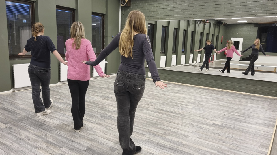 Tre unga tjejer dansar vända mot dansstudions speglar.