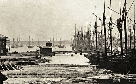 Links: Vänersborg's haven met overblijfselen van de werf bij Dyviken en het stationsgebouw in aanbouw, ca. 1865-1867.