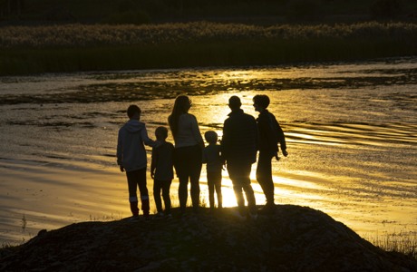 Familj med vuxna och barn som står vid sjö i soluppgång. 