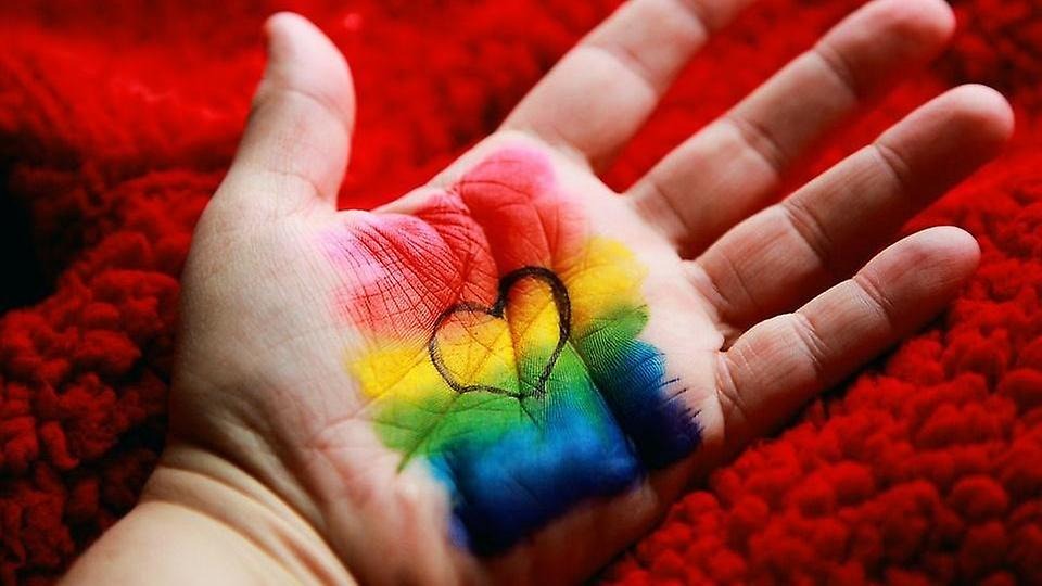 Ett hjärta i regnbågsfärgerna målat i en handflata
