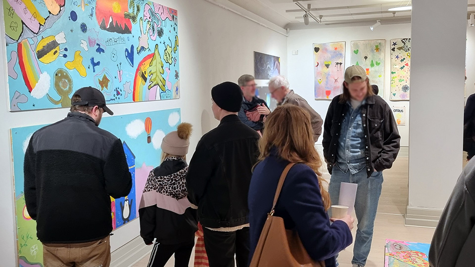 Besökare på Vänersborgs konsthall som minglar bland färgglada tavlor gjorda av barn.