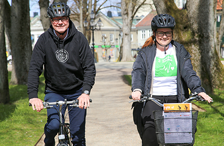 Mats Andersson och Anne Ekstedt på varsin cykel med cykelhjälm på huvudet. Grönt gräs och träd på sidorna om dem.