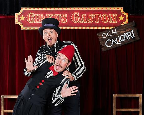 två män i klädda som cirkusdirektör och cirkusartist står framför en röd ridå