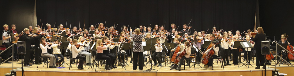 En stor orkester på barn och ungdomar spelar på scenen i Huvudnäsaulan.