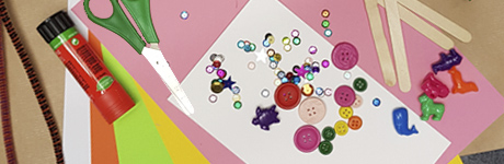 Pyssel i form av papper och pärlor i olika färger. Även ett limstift och en sax syns i bilden.