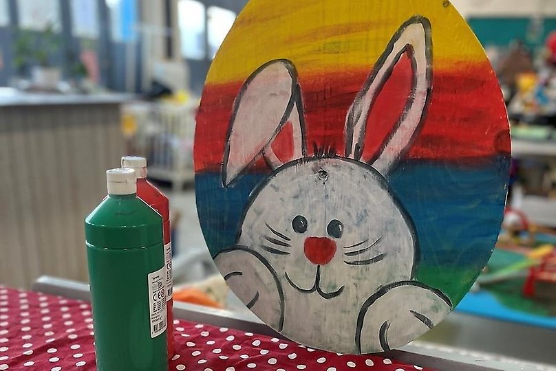 En vit kanin mot en regnbågsfärgad bakgrund målat på ett påskägg
