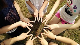 En grupp unga personer sitter i en cirkel och skapar ett mönster i mitten med sina händer.