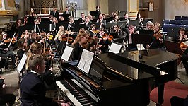 Orkester spelar i Vänersborgs kyrka. I förgrunden står en flygel.