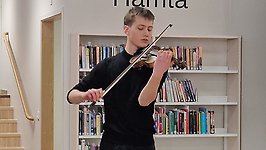 Ung kille spelar fiol bland bokhyllorna på biblioteket.